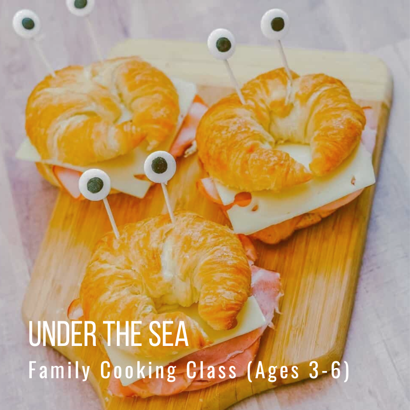 Three croissant sandwiches with googly eyes on toothpicks, on a wooden board.