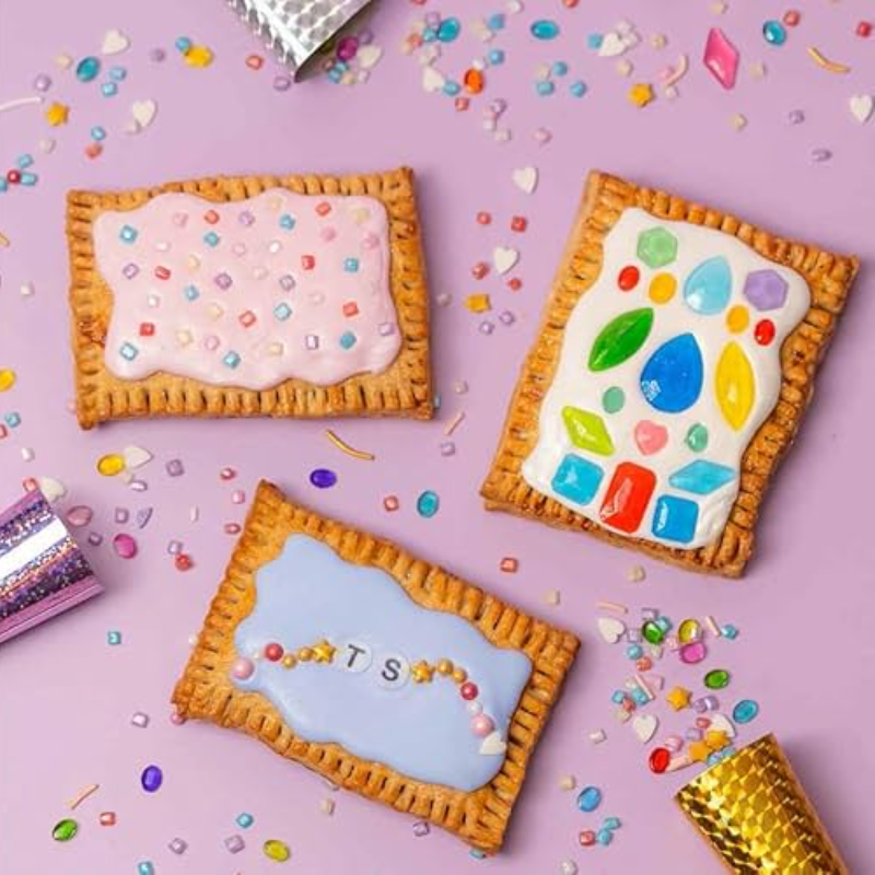 Three decorated rectangular cookies with colorful icing and sprinkles on a purple background.