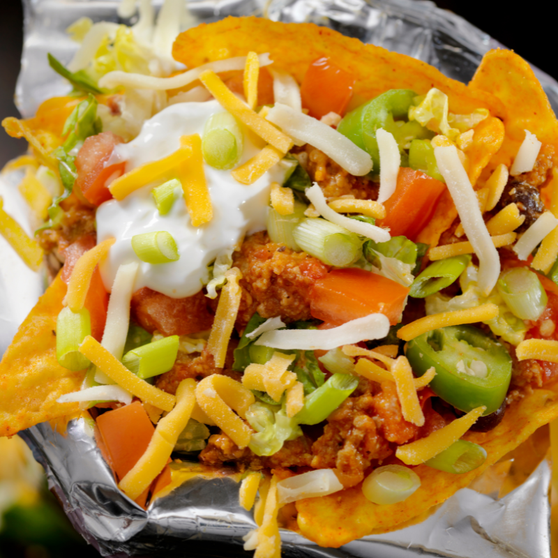 Close-up of nachos with cheese, sour cream, jalapeños, tomatoes, and lettuce on foil.