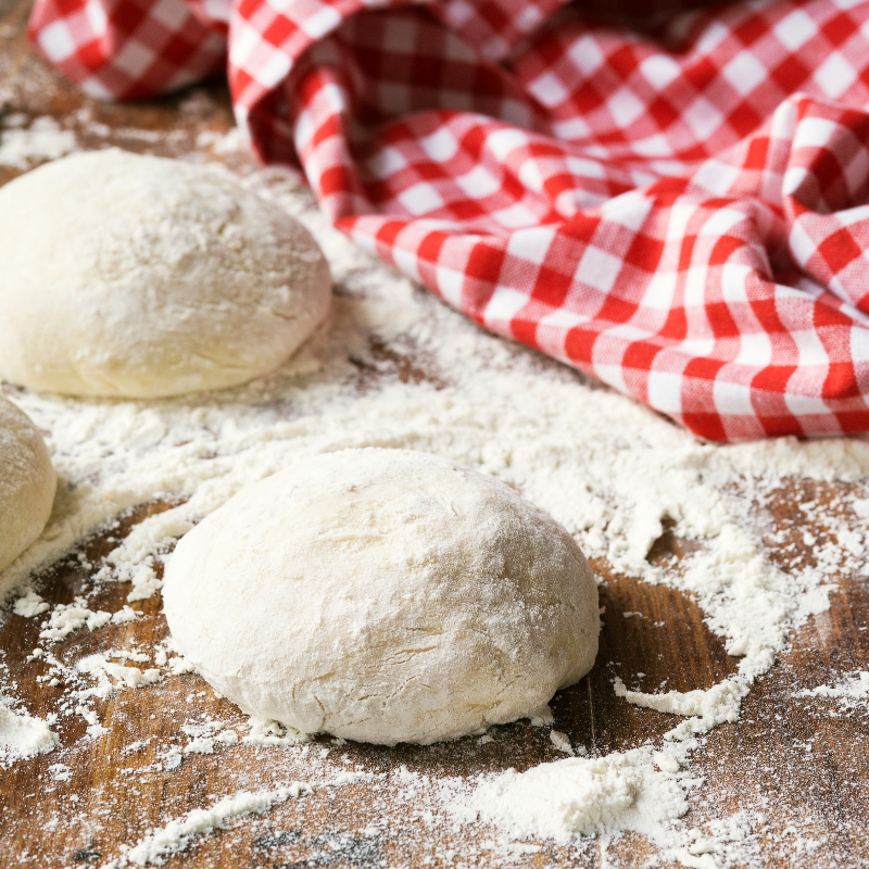 Three dough balls on a floured surface with a red gingham cloth.