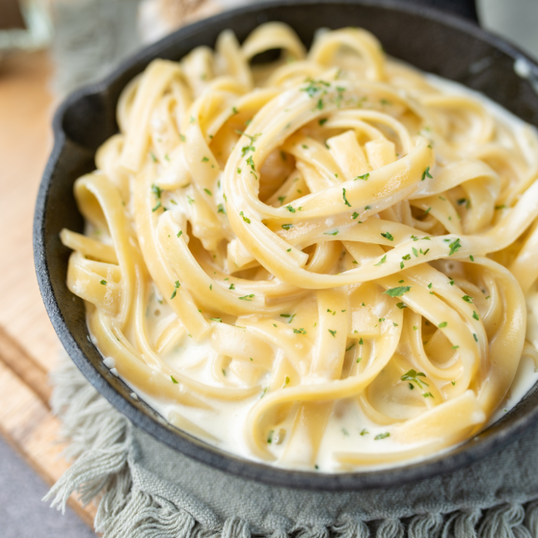 Close-up of creamy fettuccine pasta in a black bowl, garnished with herbs.