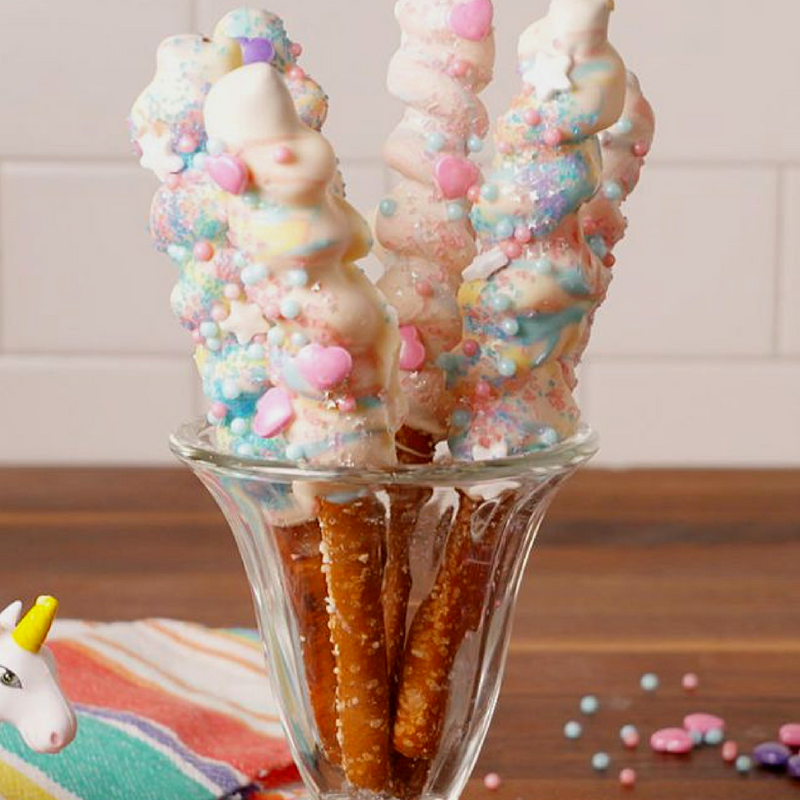 Pretzel rods coated with colorful sprinkles and icing in a glass cup.