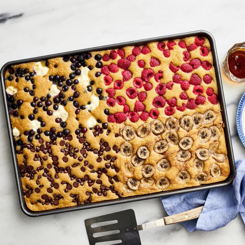 Baking tray with sections of blueberries, raspberries, bananas, and chocolate chips on a marble surface.