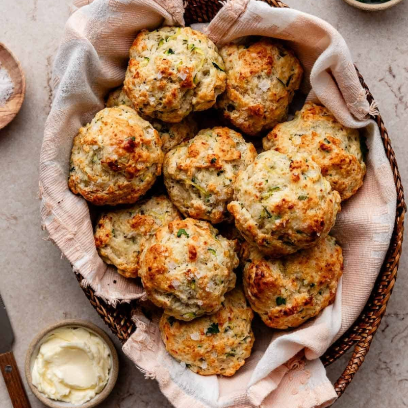 Basket of savory scones with herbs on a cloth napkin, butter on the side.