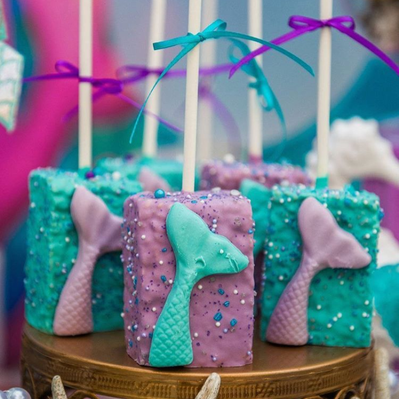 Colorful mermaid-themed cake pops with bows and tail decorations.