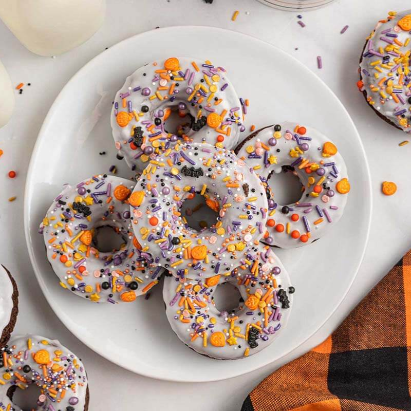 Donuts with white icing, orange and purple sprinkles on a plate.