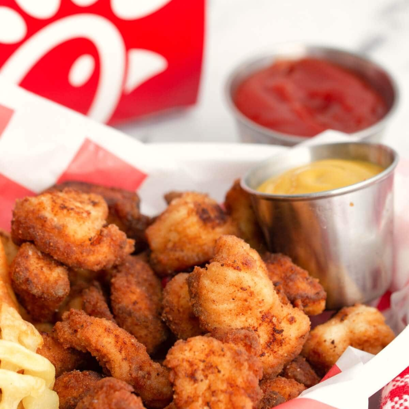 Fried chicken bites with waffle fries and dipping sauces in a basket.
