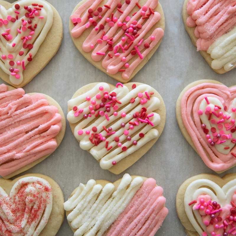 Heart-shaped cookies with pink and white frosting, topped with pink sprinkles in a grid layout.