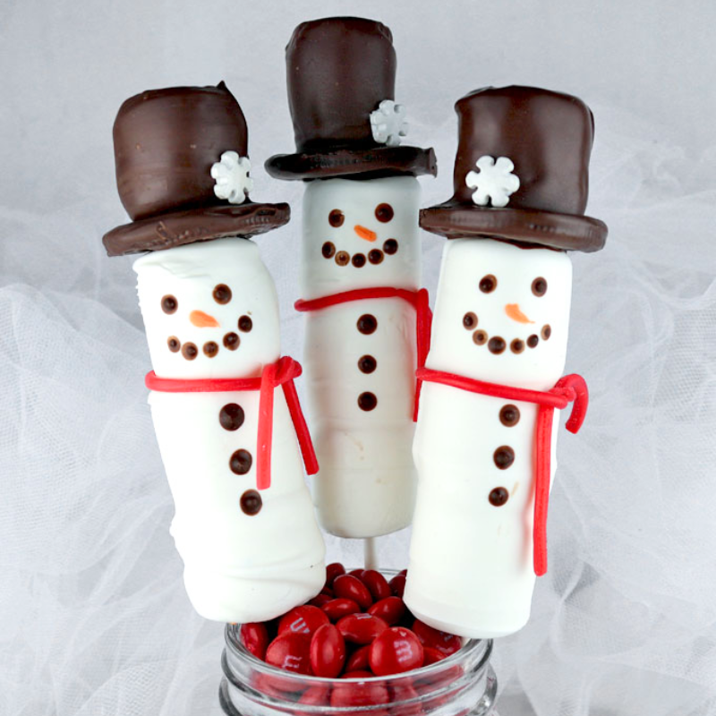 Three snowman-shaped cake pops with chocolate hats and red scarves in a jar of red candies.