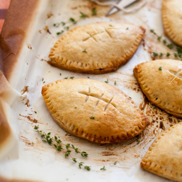 Baked hand pies shaped like footballs on parchment with herbs.