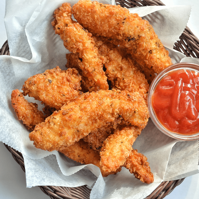 Basket of crispy fried chicken tenders with a small dish of ketchup.