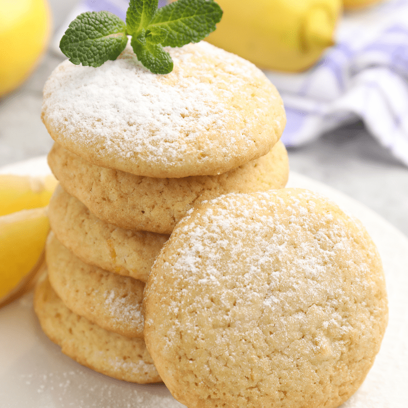 Stack of lemon cookies dusted with powdered sugar, topped with mint leaf.