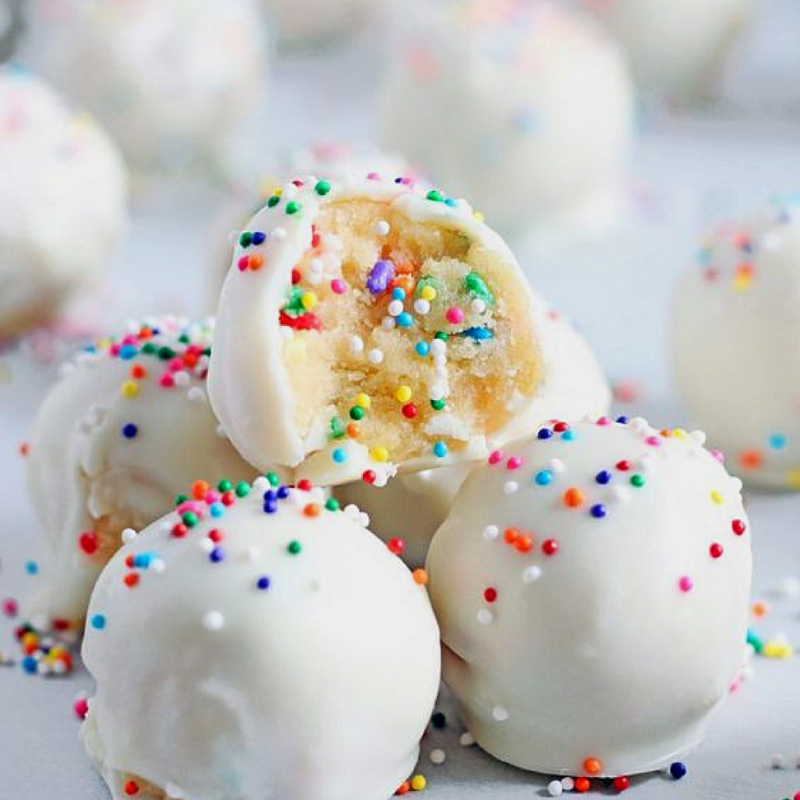 White chocolate truffles with colorful sprinkles, one bitten to reveal creamy filling.