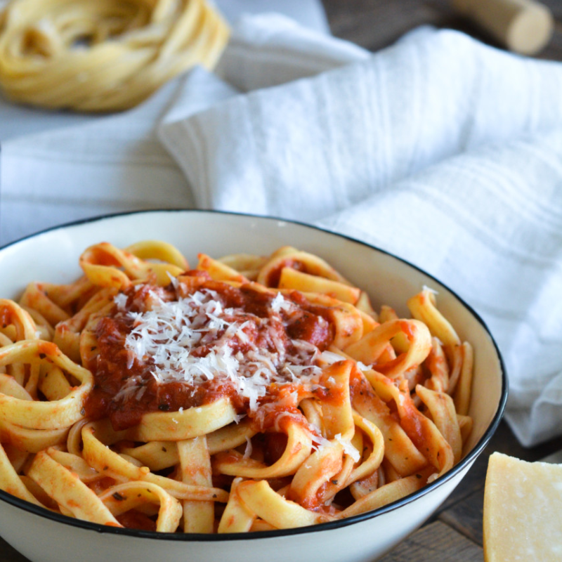 Bowl of pasta with tomato sauce and grated cheese on top.