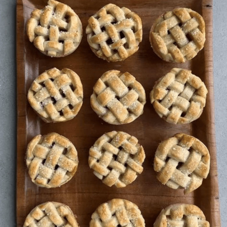 Twelve mini lattice-top pies on a wooden board.