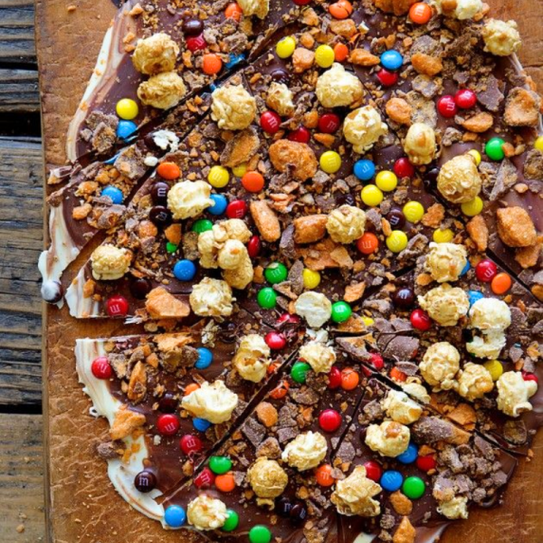 Chocolate pizza topped with popcorn, candy, and cookie pieces on a wooden surface.