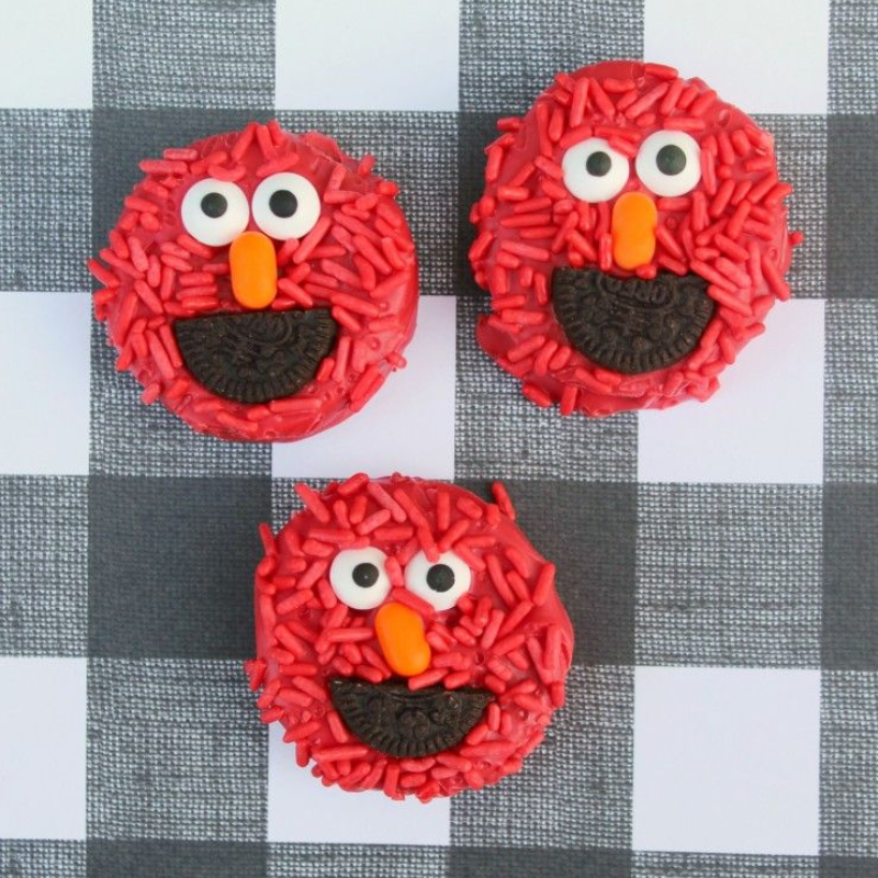 Three Elmo-themed cupcakes with red sprinkles on checkered background.