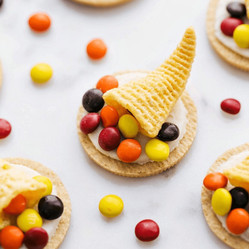 Candy cornucopia with colorful candies on crackers, scattered on a white surface.