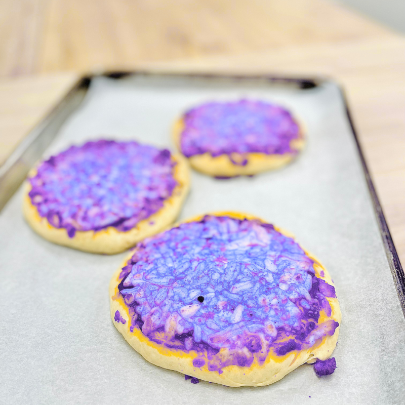 Three round pastries with purple glaze on a baking tray lined with parchment paper.