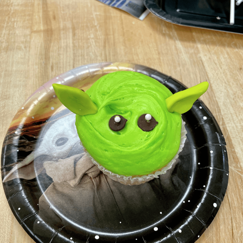Green Yoda-themed cupcake with ears and eyes on a paper plate.