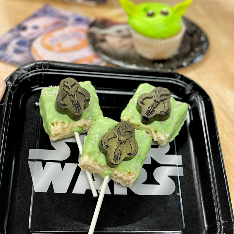 Star Wars-themed treats on a black plate, featuring green sweets with helmet decor.