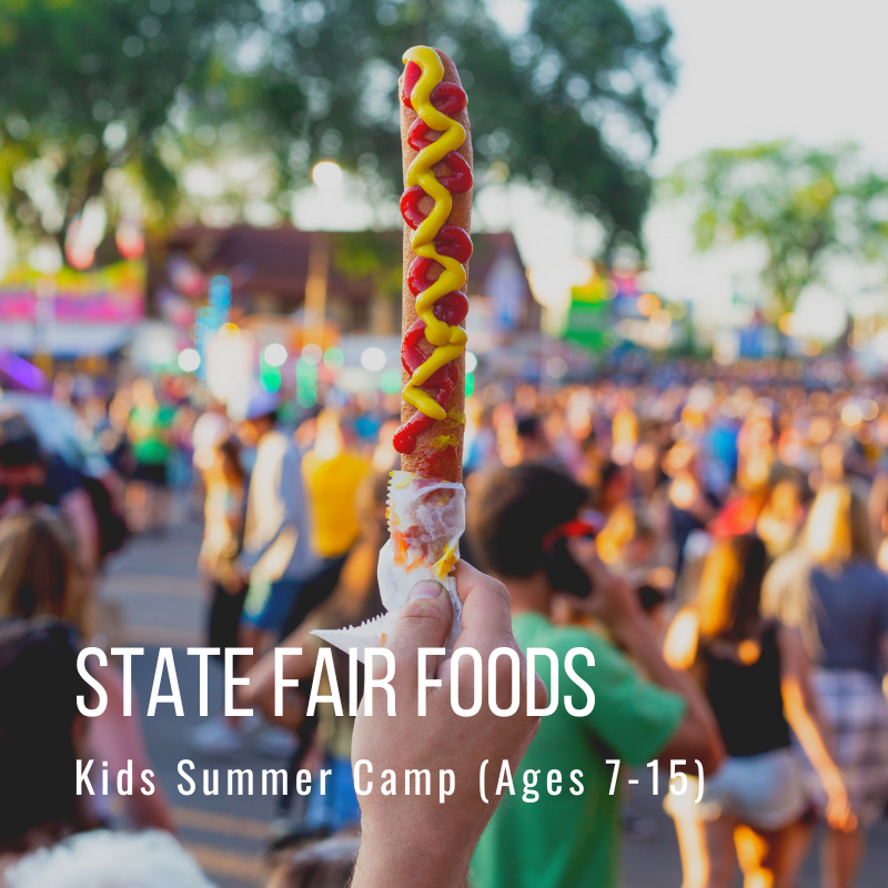 Hand holding corn dog with ketchup and mustard at a state fair.