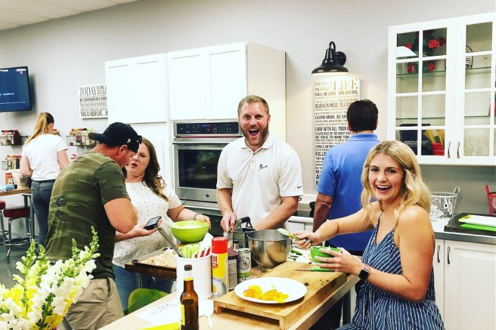 Group of people cooking and smiling together in a kitchen setting.