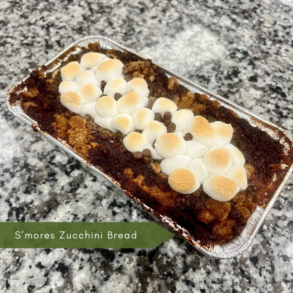 Loaf of s'mores zucchini bread topped with marshmallows in a foil tray on a countertop.
