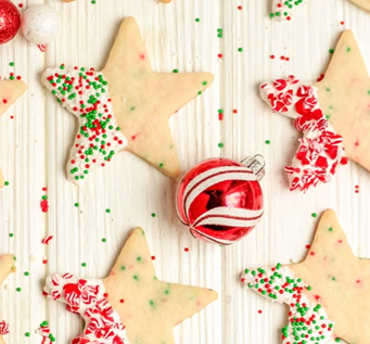 Star-shaped cookies with red, white decorations and a red ornament on a wooden surface.