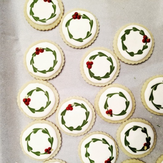 Round cookies with green wreath icing and red berries, arranged on parchment paper.