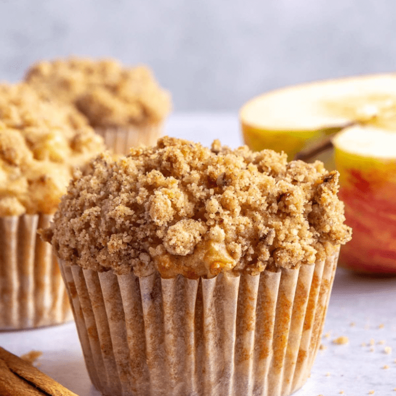 Close-up of a crumble-topped muffin with sliced apple in the background.