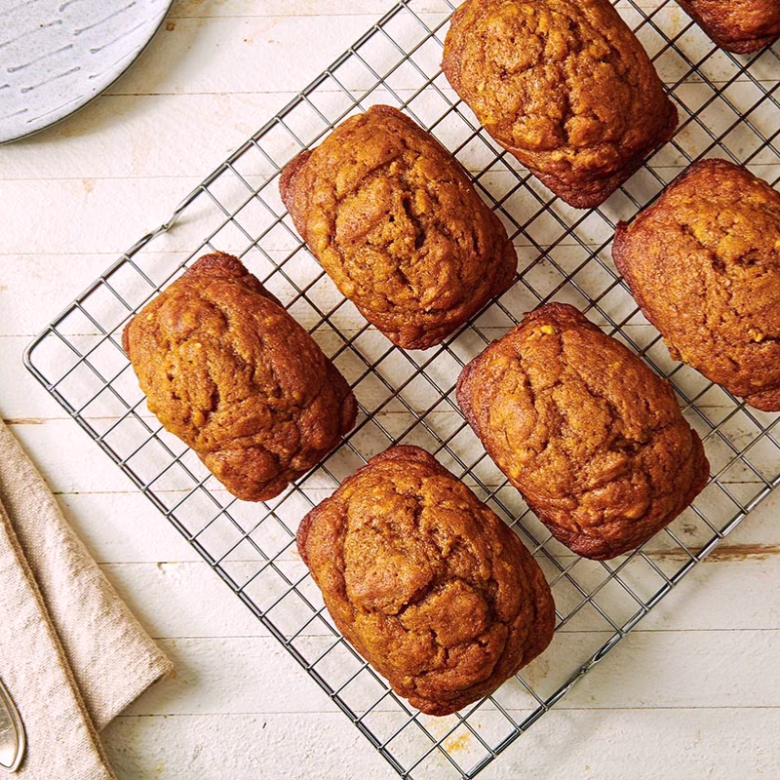 Six rectangular baked goods cooling on a wire rack on a white wooden surface.