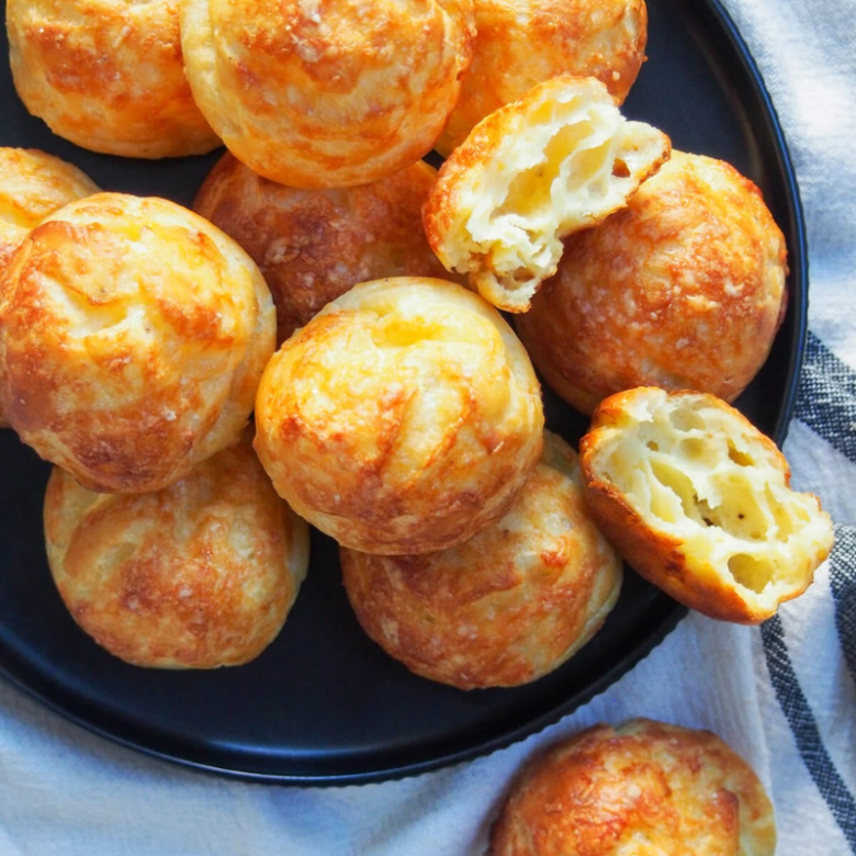 Black plate with round, golden-brown cheese puffs on a cloth.