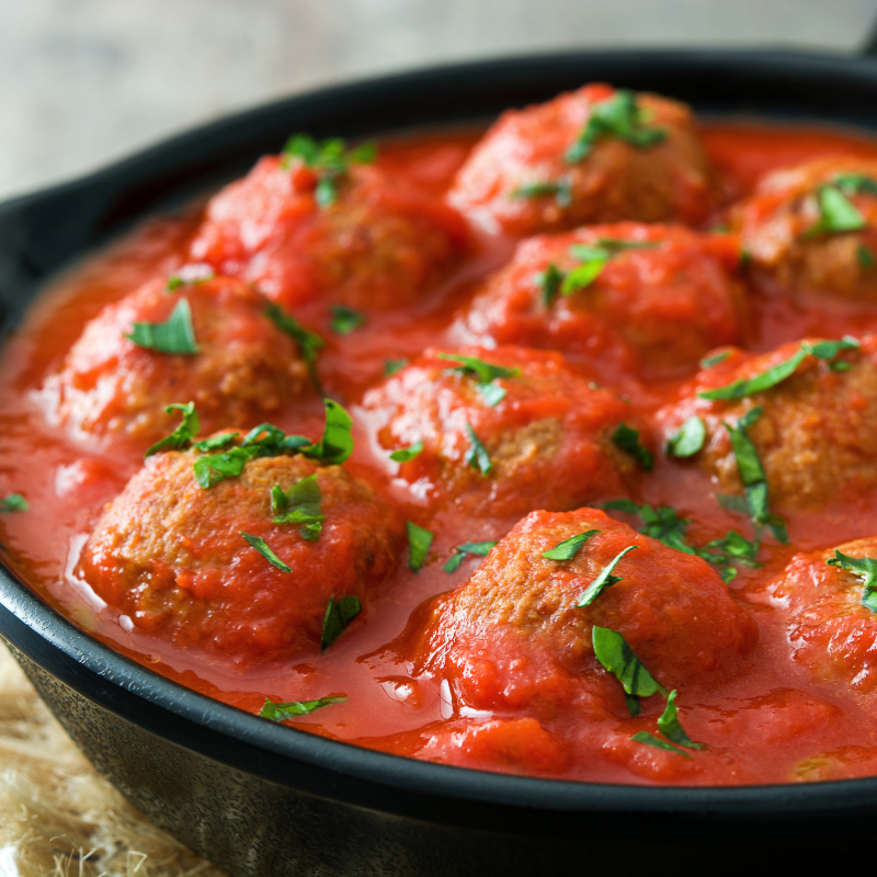 Meatballs in tomato sauce garnished with herbs in a black pan.