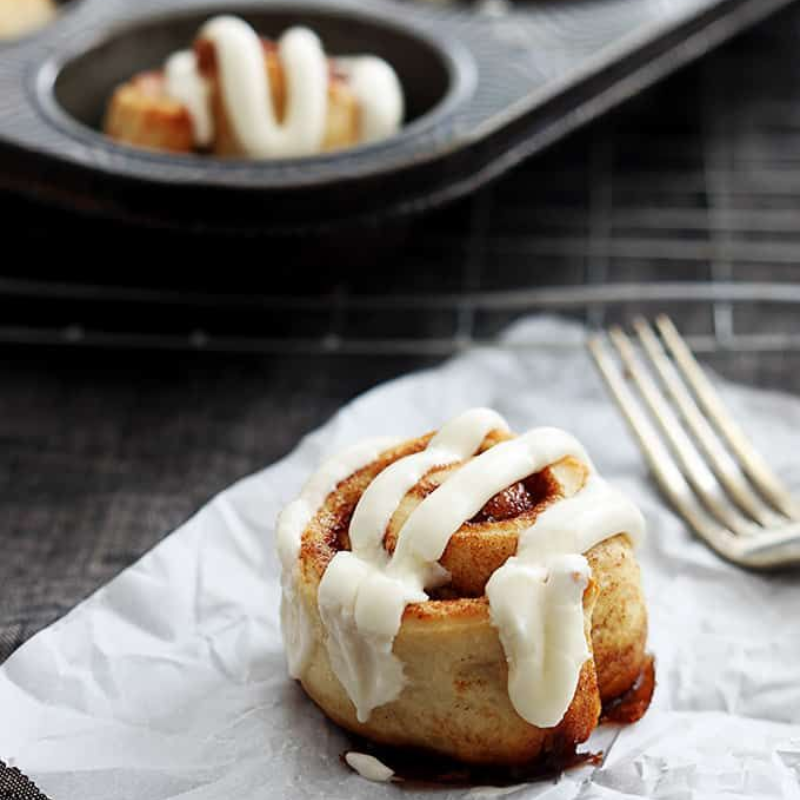 Iced cinnamon rolls with muffin tin on table.
