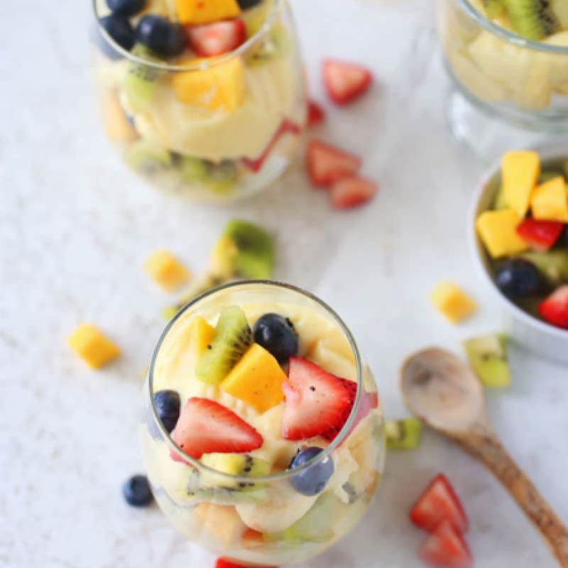 Fruit salad in glasses with strawberries, blueberries, kiwi, and mango on a white surface.