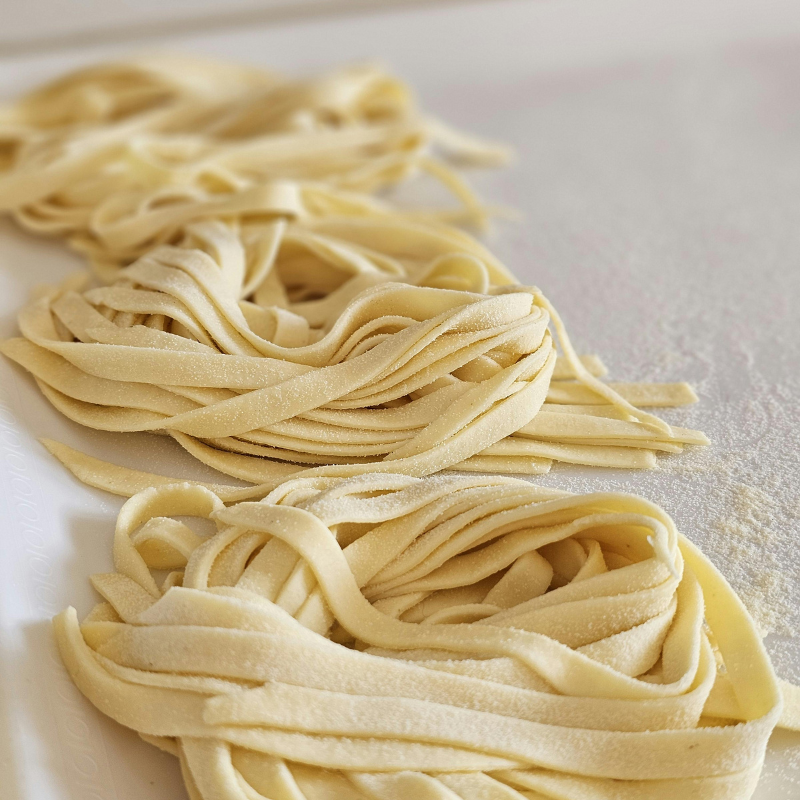 Freshly made fettuccine pasta arranged in nests on a floured surface.