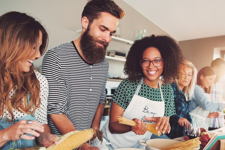 Group of smiling friends cooking together in a kitchen, preparing various ingredients.