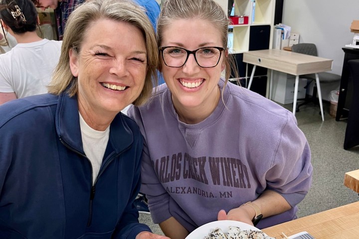 Two people smiling and holding plates of sushi in a kitchen setting.