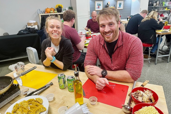 Two people smiling at a table with food, surrounded by others in a casual dining setting.