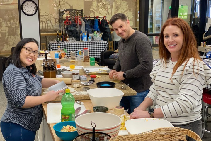 Three people smiling and preparing food in a kitchen setting.