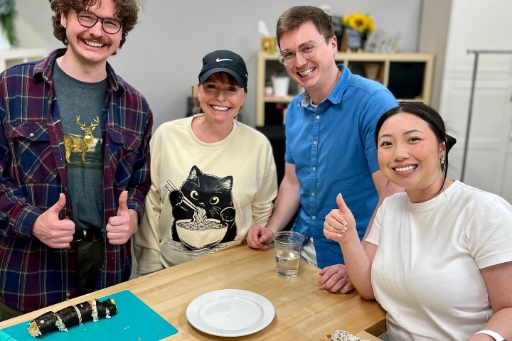 Four people smiling in a kitchen with sushi rolls on the counter.