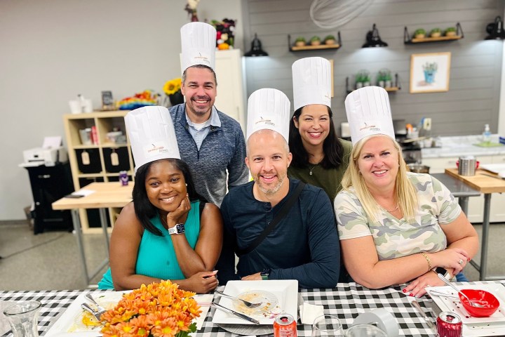 Five people smiling and wearing chef hats at a dining table.