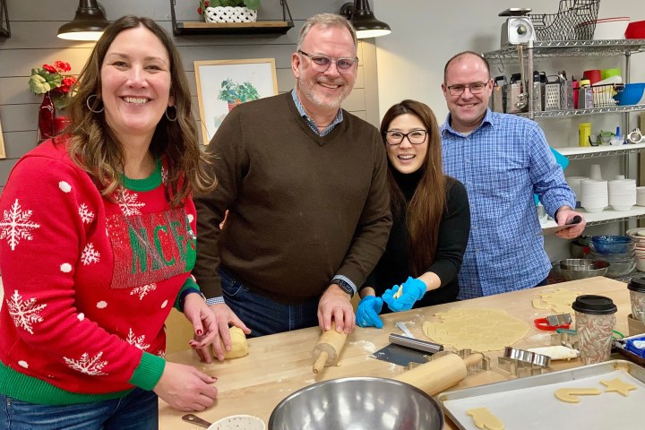 Four people smiling while making cookie dough in a kitchen.