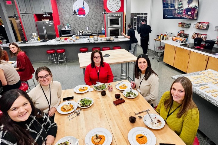 Five people dining at a table with plates of food in a bright kitchen setting.