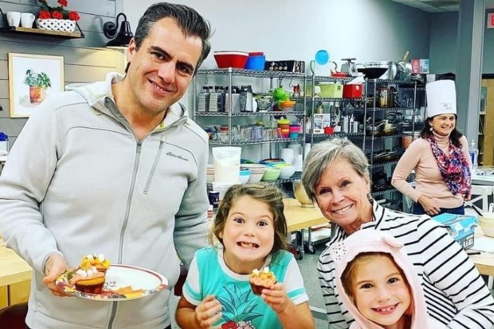 Smiling group with cupcakes in a kitchen, shelves with kitchenware in the background.