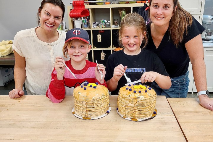 Two adults and two kids smiling with pancake stack cakes on a table.