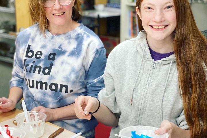 Two people smile while decorating cookies at a table with colorful icing and cookie shapes.