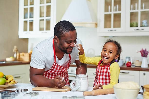 Man and child in aprons laughing while baking in a kitchen.