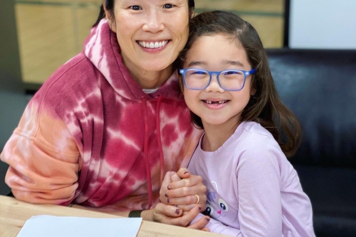 Smiling woman in red hoodie and girl with glasses at a table with candy.